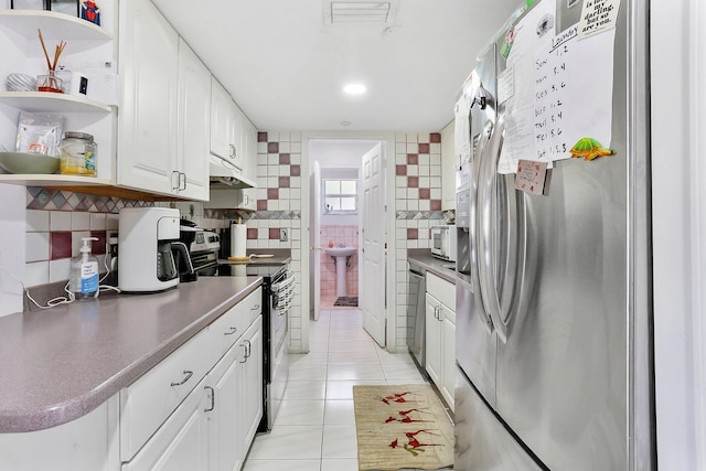 kitchen with light tile patterned flooring, tile walls, white cabinets, decorative backsplash, and stainless steel appliances