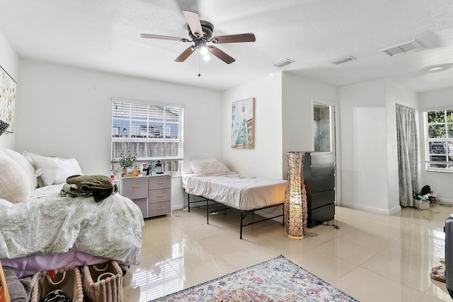 bedroom featuring ceiling fan, light tile patterned floors, and a textured ceiling