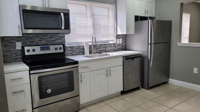 kitchen with appliances with stainless steel finishes, tasteful backsplash, sink, white cabinets, and light tile patterned floors