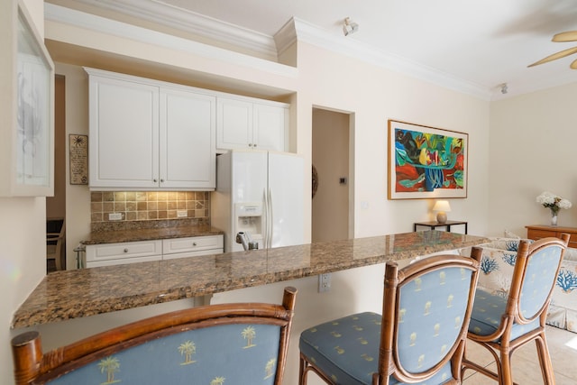 kitchen featuring white cabinetry, ornamental molding, dark stone counters, and white fridge with ice dispenser