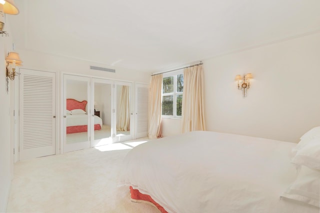 bedroom with two closets, light colored carpet, and french doors