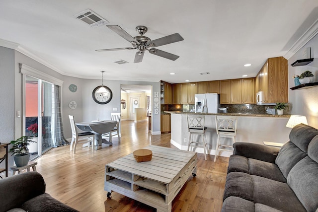 living room with ornamental molding, light hardwood / wood-style floors, and ceiling fan