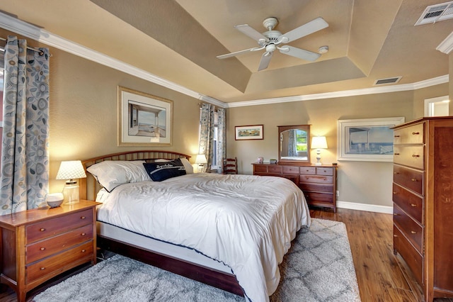 bedroom with crown molding, ceiling fan, wood-type flooring, and a raised ceiling