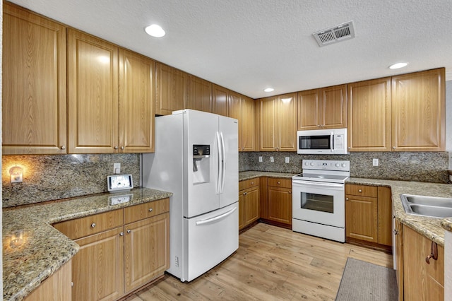 kitchen featuring sink, white appliances, backsplash, light stone counters, and light wood-type flooring