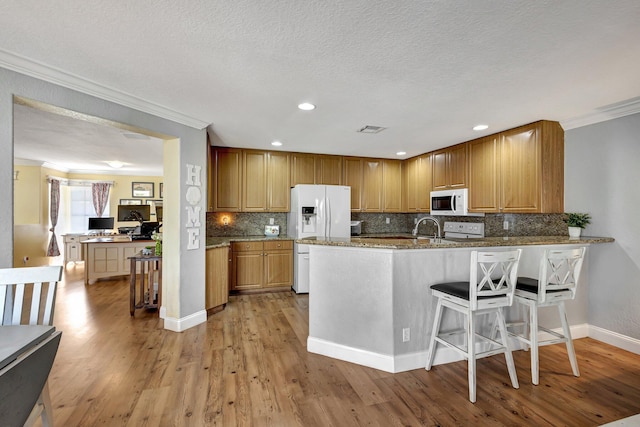 kitchen with crown molding, white appliances, a breakfast bar area, light hardwood / wood-style floors, and kitchen peninsula