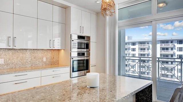 kitchen with double oven, decorative backsplash, light stone countertops, and white cabinets