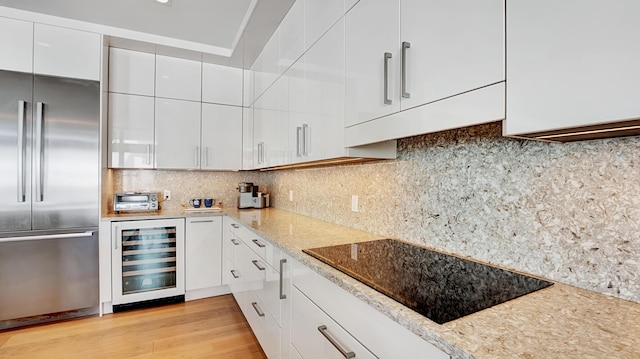 kitchen with black electric stovetop, light stone countertops, white cabinets, beverage cooler, and stainless steel built in fridge