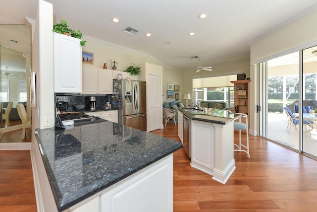 kitchen with ceiling fan, appliances with stainless steel finishes, ornamental molding, white cabinets, and a kitchen island