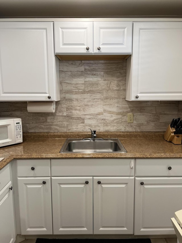 kitchen featuring tasteful backsplash, white cabinetry, and sink