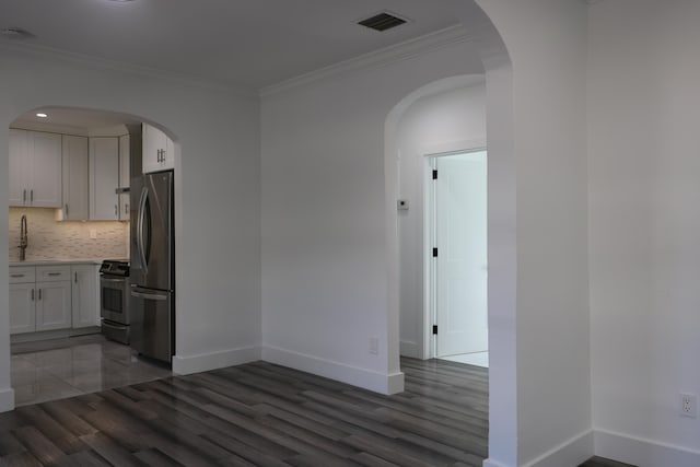 interior space with appliances with stainless steel finishes, white cabinetry, backsplash, dark hardwood / wood-style flooring, and ornamental molding