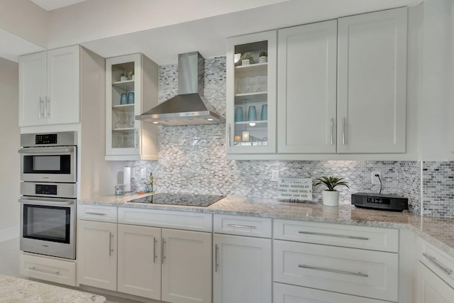 kitchen with white cabinetry, double oven, backsplash, black electric cooktop, and wall chimney exhaust hood