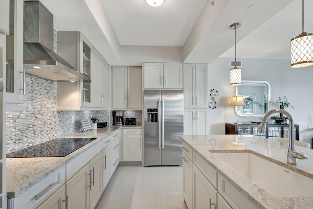 kitchen featuring pendant lighting, sink, stainless steel fridge, black electric cooktop, and wall chimney exhaust hood