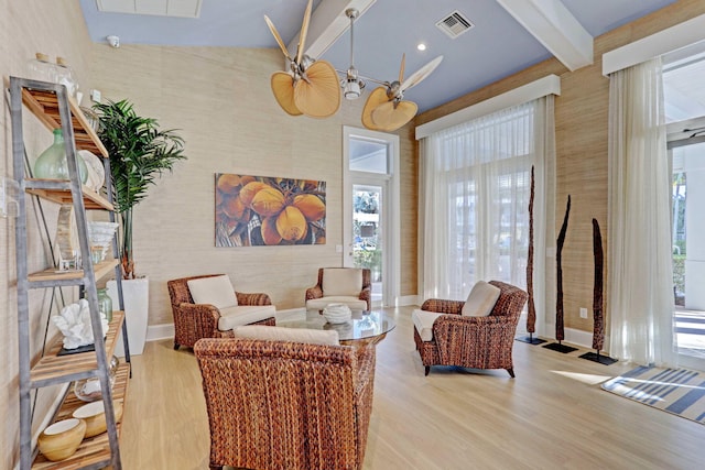 sitting room featuring a towering ceiling, beam ceiling, and light hardwood / wood-style floors