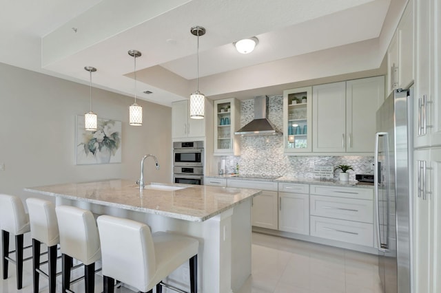 kitchen featuring wall chimney range hood, sink, appliances with stainless steel finishes, white cabinetry, and a raised ceiling