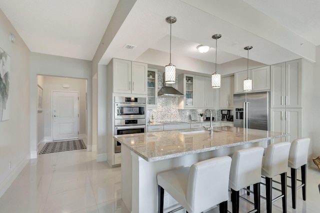 kitchen with appliances with stainless steel finishes, light stone countertops, decorative backsplash, and wall chimney range hood