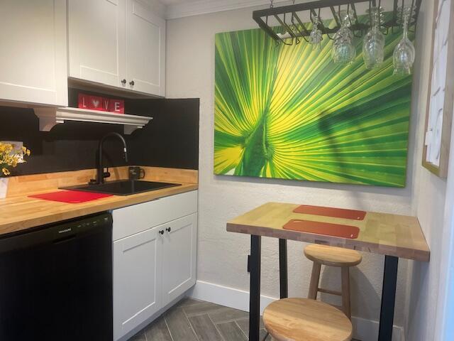 kitchen with ornamental molding, black dishwasher, sink, and white cabinets