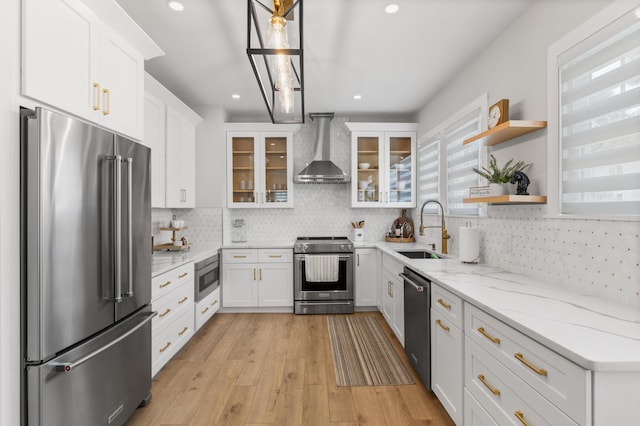 kitchen featuring wall chimney exhaust hood, sink, appliances with stainless steel finishes, pendant lighting, and white cabinets