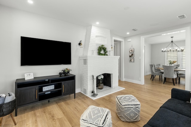 living room featuring a brick fireplace, an inviting chandelier, and light hardwood / wood-style flooring