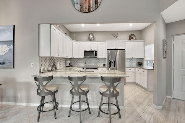 kitchen with stainless steel appliances, a breakfast bar, light stone countertops, and white cabinets