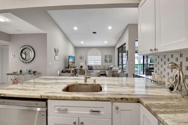 kitchen with vaulted ceiling, sink, white cabinets, stainless steel dishwasher, and light stone counters