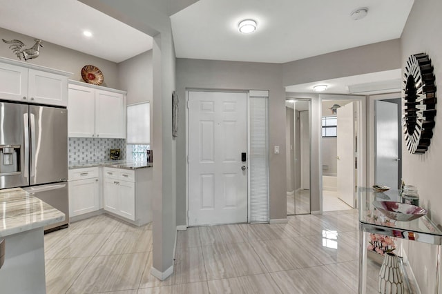 kitchen featuring white cabinetry, decorative backsplash, stainless steel fridge, and light stone countertops