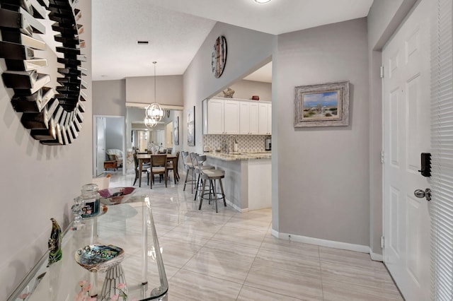 interior space with a breakfast bar, decorative light fixtures, white cabinetry, lofted ceiling, and an inviting chandelier