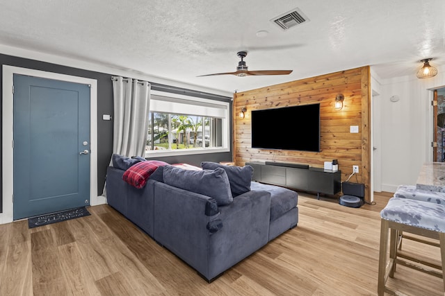 living room with ceiling fan, hardwood / wood-style floors, a textured ceiling, and wood walls