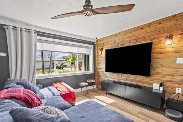 living room featuring a textured ceiling, wooden walls, ceiling fan, and light wood-type flooring