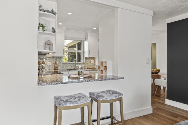 kitchen with sink, dark stone countertops, white cabinets, dark hardwood / wood-style flooring, and backsplash