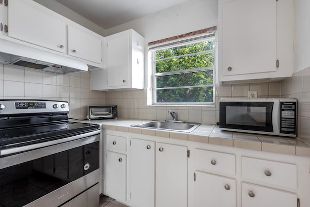 kitchen featuring appliances with stainless steel finishes, sink, tile counters, and white cabinets