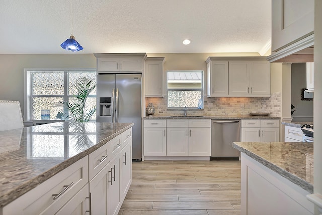 kitchen featuring stainless steel appliances, light stone countertops, sink, and decorative light fixtures