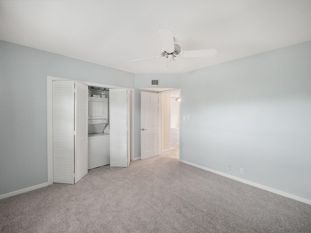 unfurnished bedroom featuring light carpet, a closet, stacked washer and clothes dryer, and ceiling fan