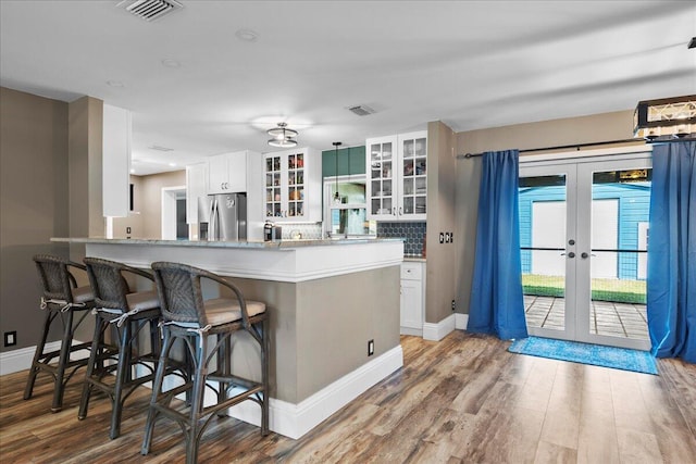 kitchen with stainless steel fridge, white cabinets, a kitchen breakfast bar, kitchen peninsula, and french doors