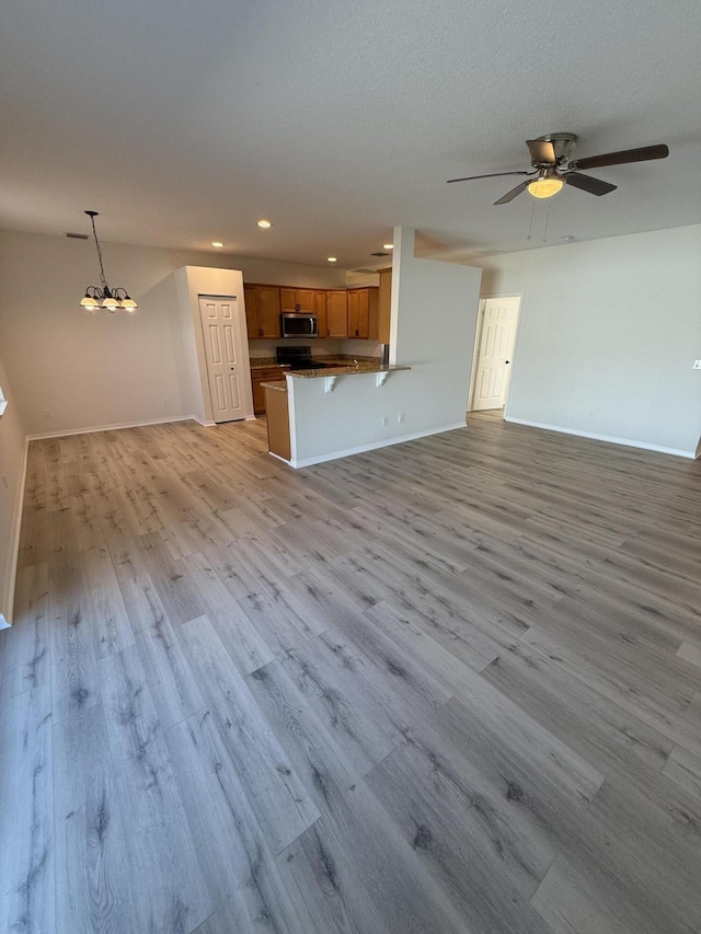 unfurnished living room featuring ceiling fan with notable chandelier and light hardwood / wood-style flooring