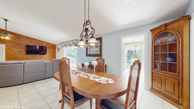 dining room featuring ceiling fan, wooden walls, a textured ceiling, and light tile patterned floors