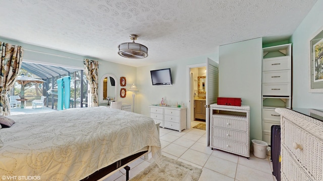 bedroom featuring ensuite bathroom, light tile patterned floors, access to exterior, and a textured ceiling