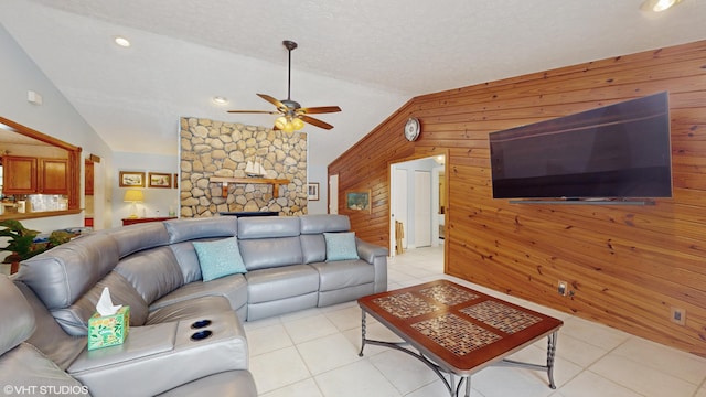 living room featuring lofted ceiling, light tile patterned floors, ceiling fan, wooden walls, and a textured ceiling