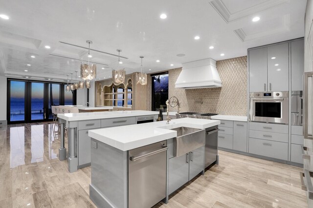 kitchen with decorative light fixtures, a water view, a sink, light countertops, and a large island with sink