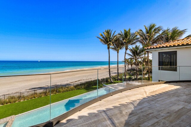 wooden deck featuring a view of the beach, a water view, and fence