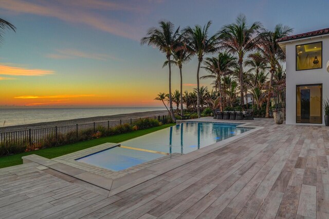 pool at dusk featuring a patio area, a water view, fence, and a fenced in pool