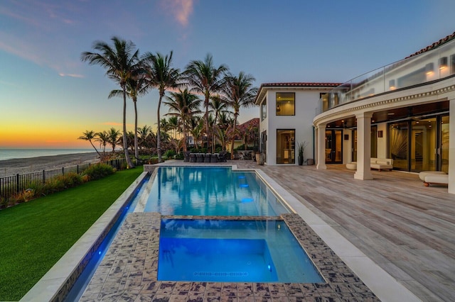 view of pool with ceiling fan, a water view, fence, a pool with connected hot tub, and a yard