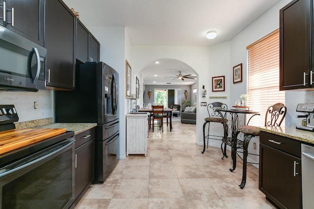 kitchen with dark brown cabinetry, tasteful backsplash, light stone counters, electric range, and ceiling fan