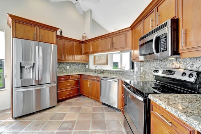 kitchen with lofted ceiling, sink, appliances with stainless steel finishes, light stone countertops, and backsplash