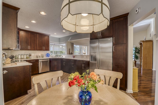 6938 Touchstone Cir, Palm Beach Gardens, FL 33418 - kitchen featuring appliances with stainless steel finishes, a textured ceiling, tasteful backsplash, dark brown cabinets, and light wood-type flooring