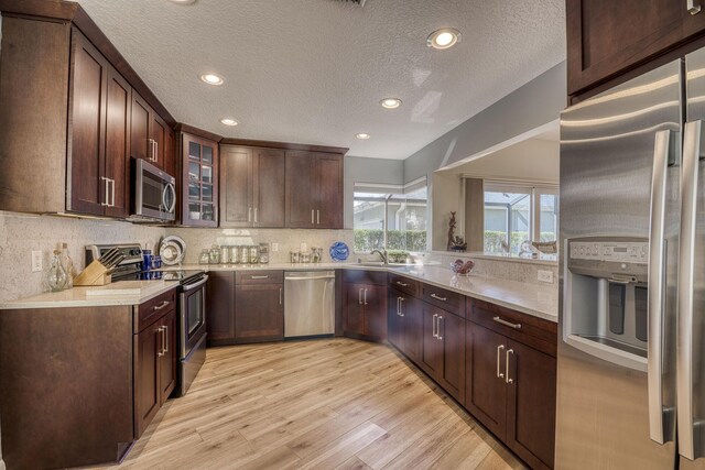 6938 Touchstone Cir, Palm Beach Gardens, FL 33418 - kitchen featuring stainless steel appliances, a sink, glass insert cabinets, a textured ceiling, and light wood finished floors