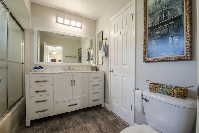 full bathroom featuring toilet, a textured ceiling, vanity, enclosed tub / shower combo, and hardwood / wood-style floors