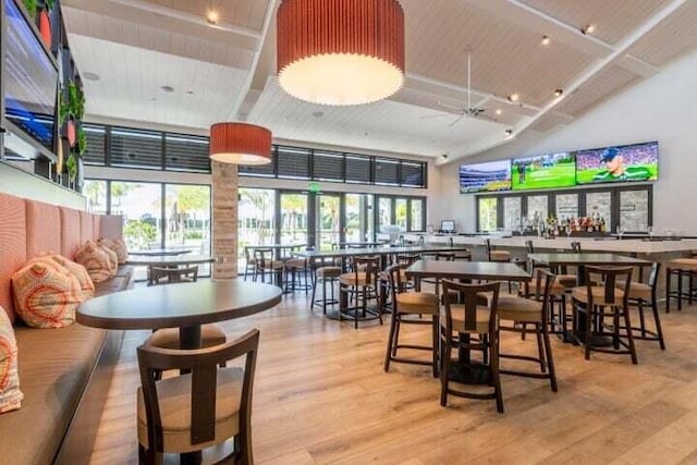 dining space with a high ceiling, beamed ceiling, ceiling fan, and light hardwood / wood-style flooring