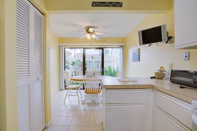 kitchen with light tile patterned floors, kitchen peninsula, white cabinets, and ceiling fan