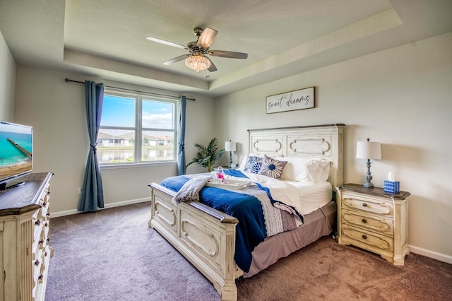 carpeted bedroom with ceiling fan and a raised ceiling