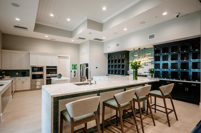 kitchen with white cabinetry, sink, a breakfast bar area, a large island, and a tray ceiling